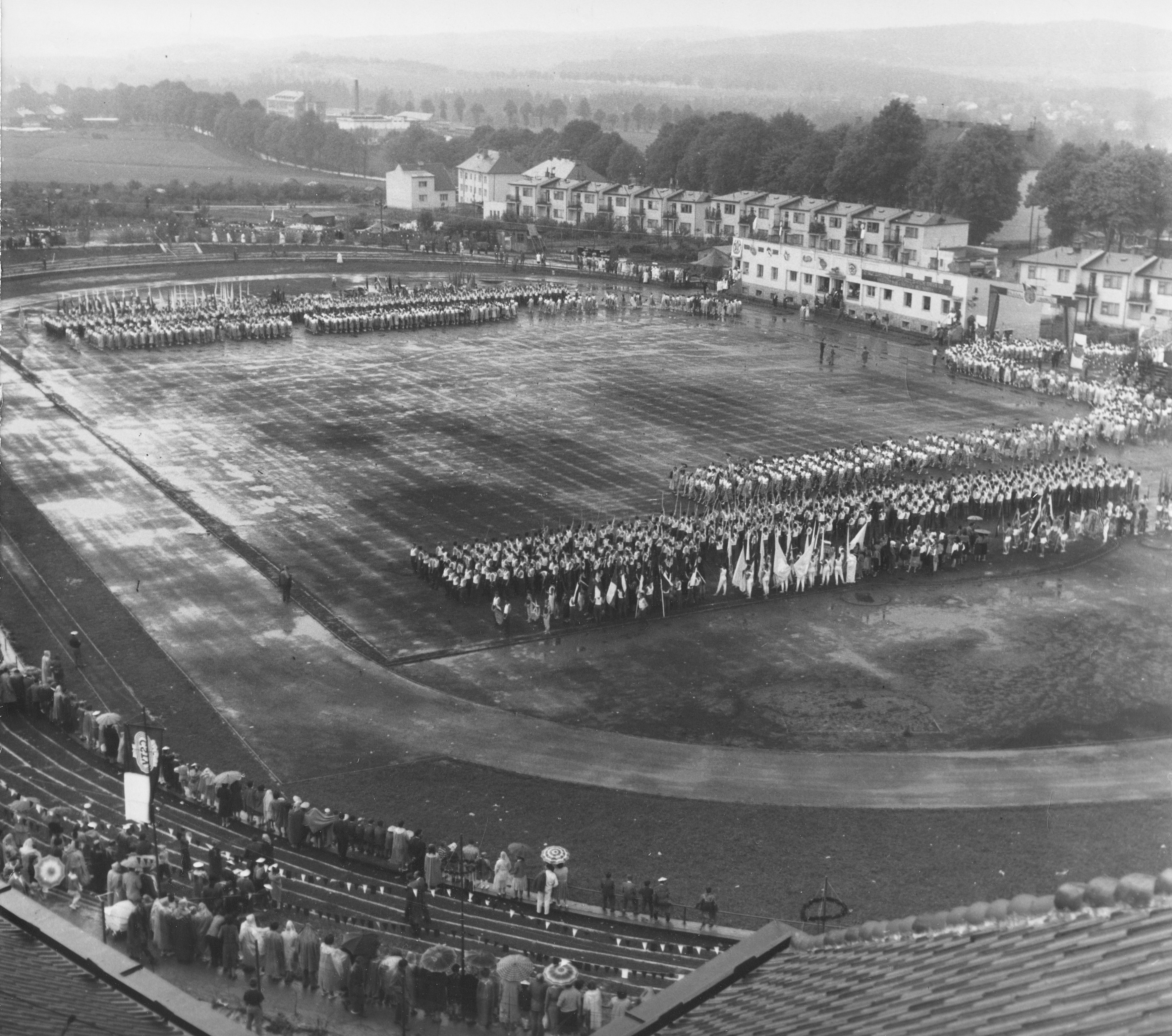 Cvičenci nastupují na plochu stadionu Spartak. Celkový pohled s diváky, kteří neváhali přijít i za deštivého počasí. Reprofoto: poskytl Stanislav Jelínek        