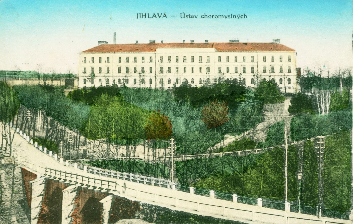 Hlavní budova Ústavu choromyslných v Jihlavě kolem roku 1900 na kolorované pohlednici. V popředí starý Brněnský most